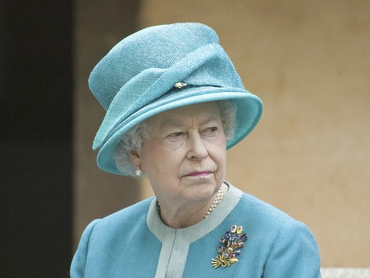 क्वीन एलिजाबेथ द्वितीय हल्की नीली टोपी और पोशाक में स्थिर दिख रही हैं।