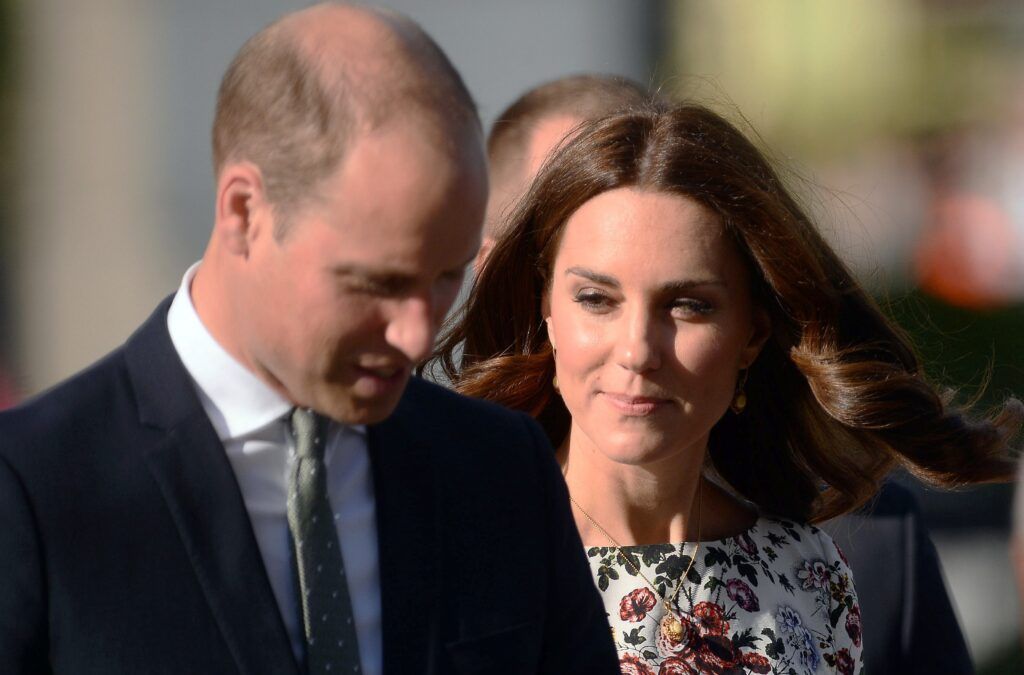 Prinz William, der einen dunklen Anzug und eine grüne Krawatte trägt, geht mit Kate Middleton in einem Blumenkleid spazieren
